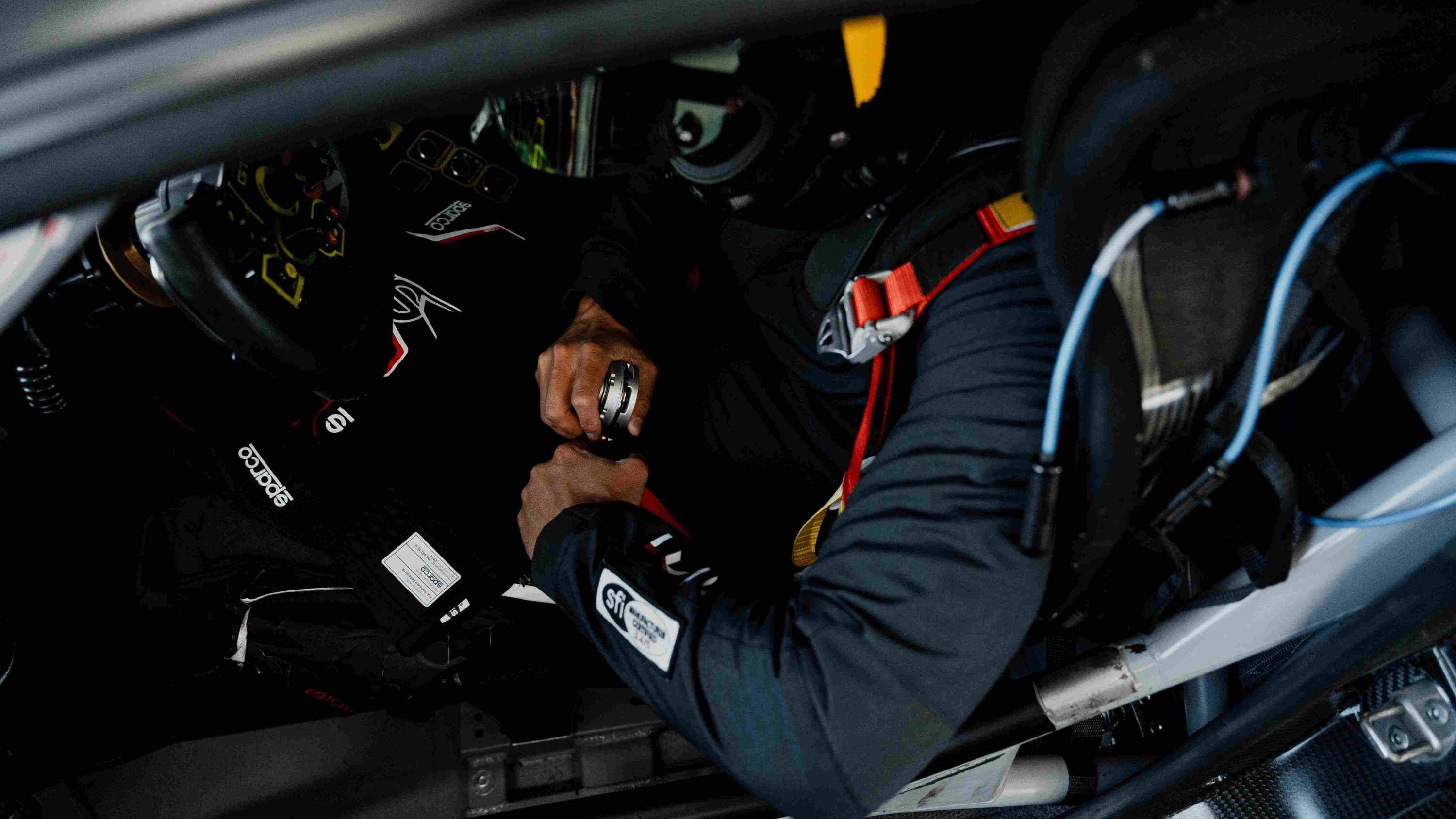 Driver wearing the LVRY DRVR racing suit buckling into a race seat, showcasing SFI-certified safety features and cockpit-ready design.