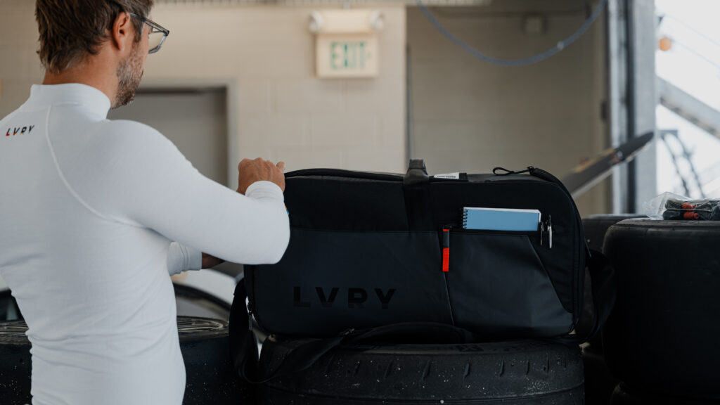 LVRY CRRY racing gear bag on stacked race tires—driver organizing track-day equipment in the paddock.