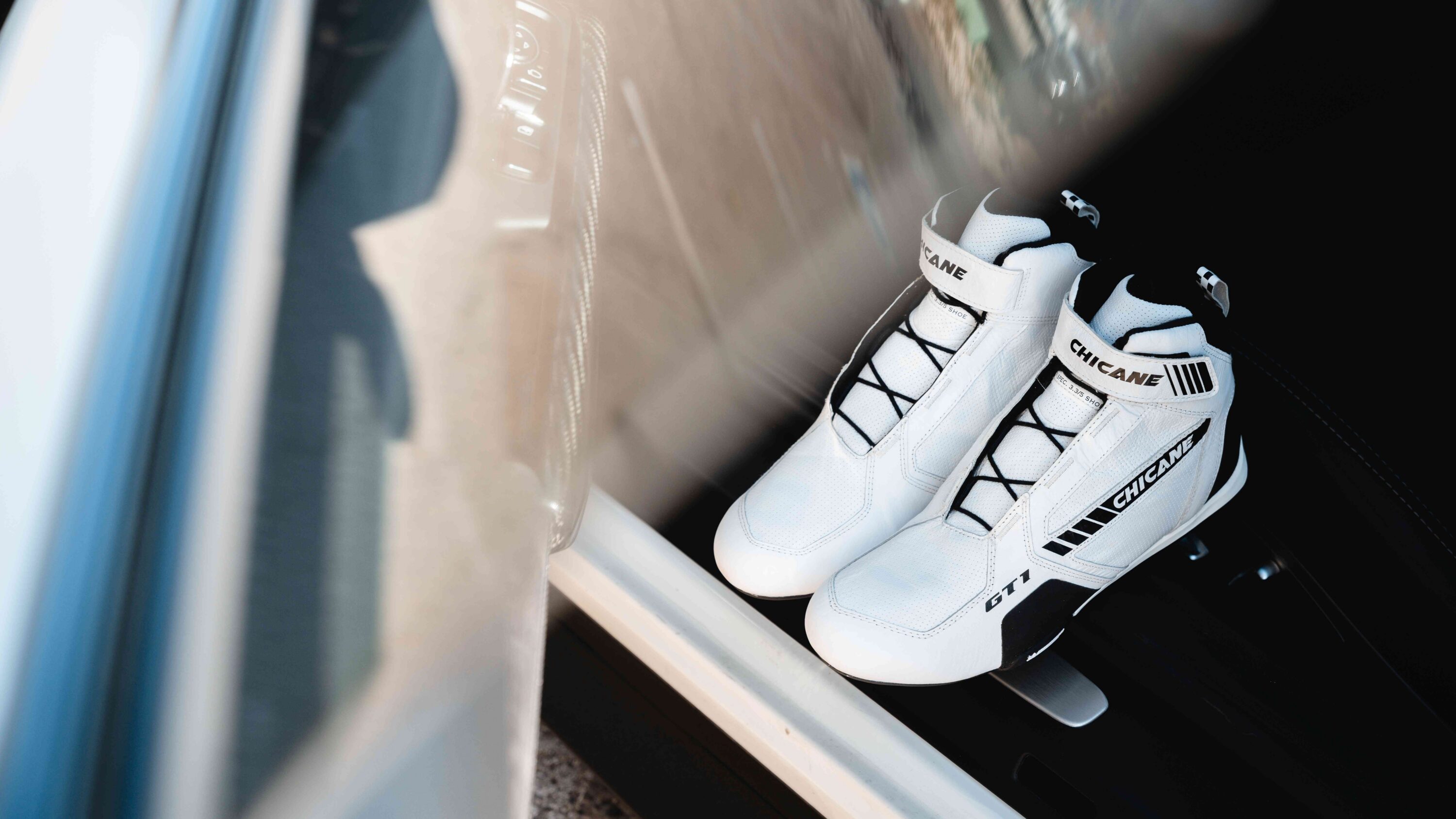 GT1 lightweight professional racing shoes in white with kangaroo leather construction and Michelin performance soles placed in a race car cockpit, designed for maximum pedal feel, breathability, fire-resistant protection, and precision control for competitive and advanced drivers.