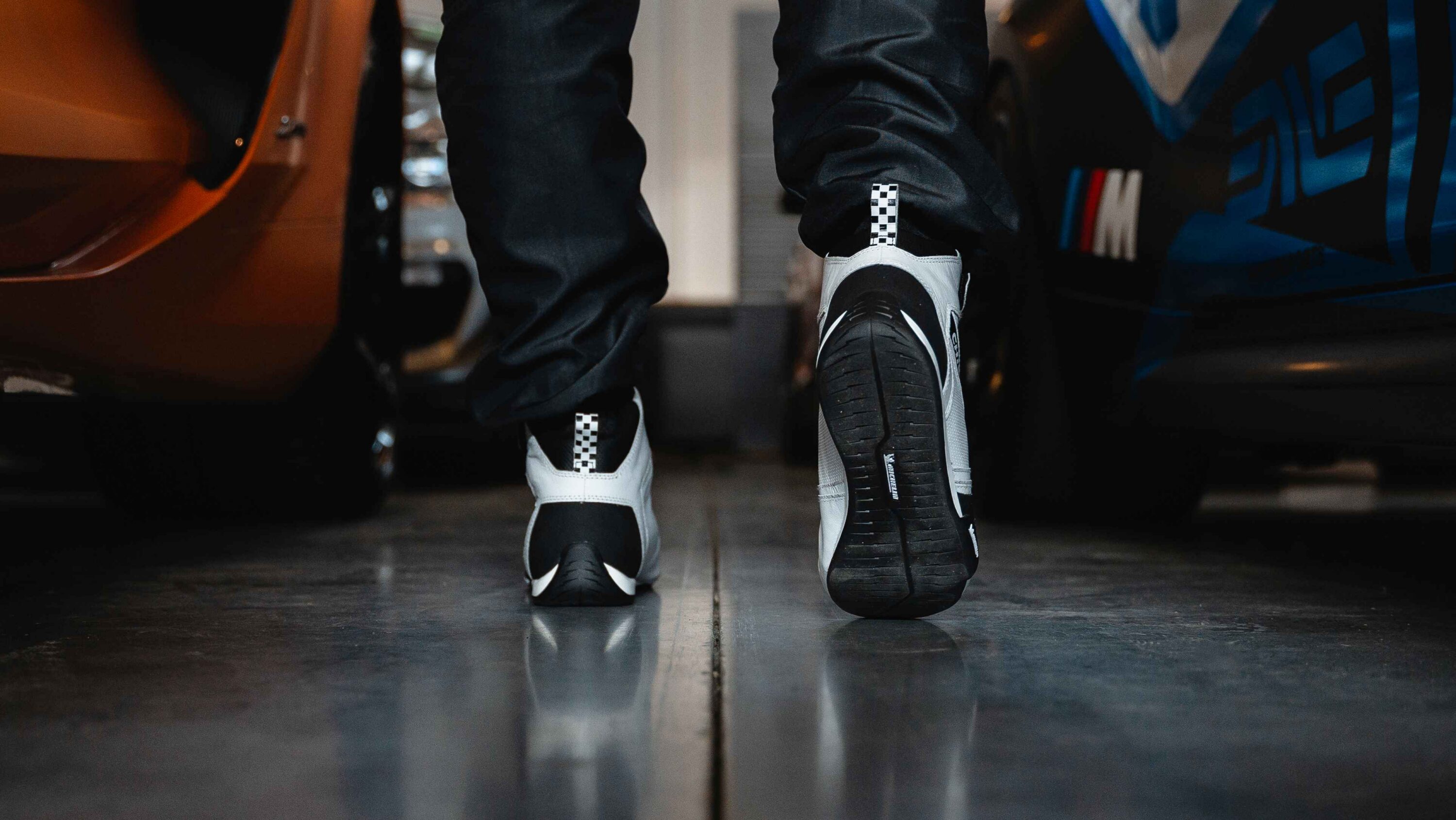 Driver walking between race cars wearing LVRY Chicane GT1 motorsport shoes with Michelin sole for enhanced pedal feel and grip.