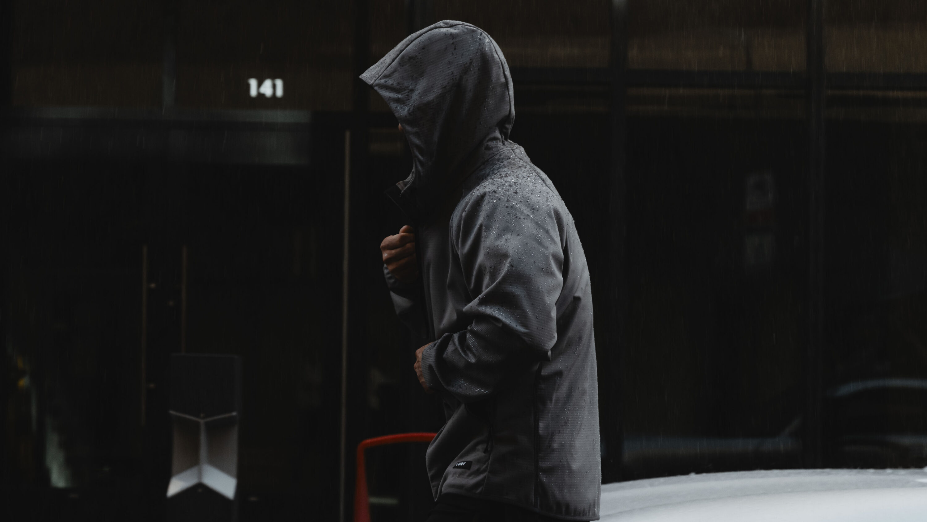 Side view of person wearing LVRY Pace water-resistant jacket with hood, raindrops on fabric.