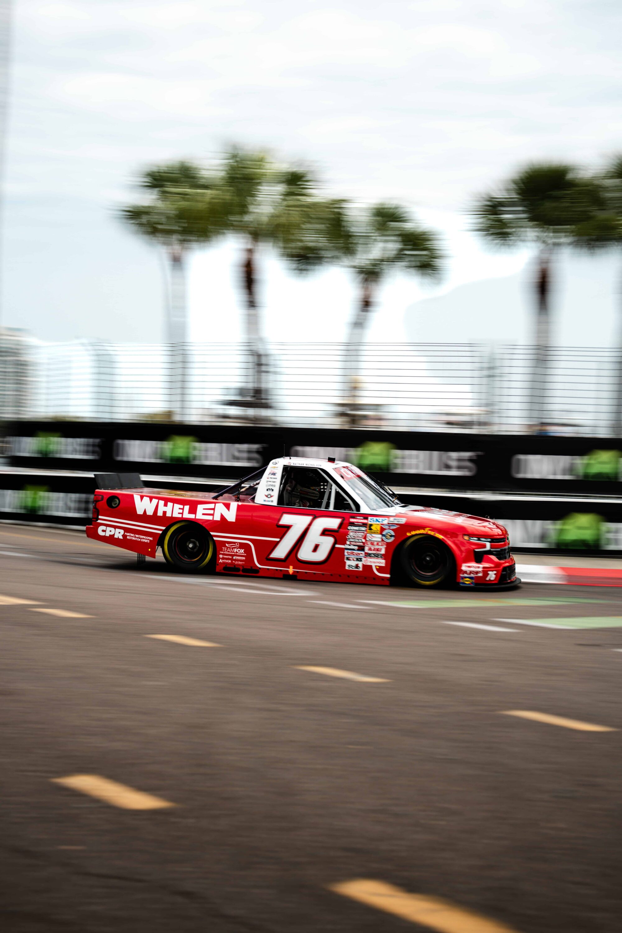 Nathan Nicholson driving the No. 76 Whelen Chevrolet in the NASCAR Craftsman Truck Series on the streets of St. Petersburg, racing past palm trees on the downtown street circuit road course.