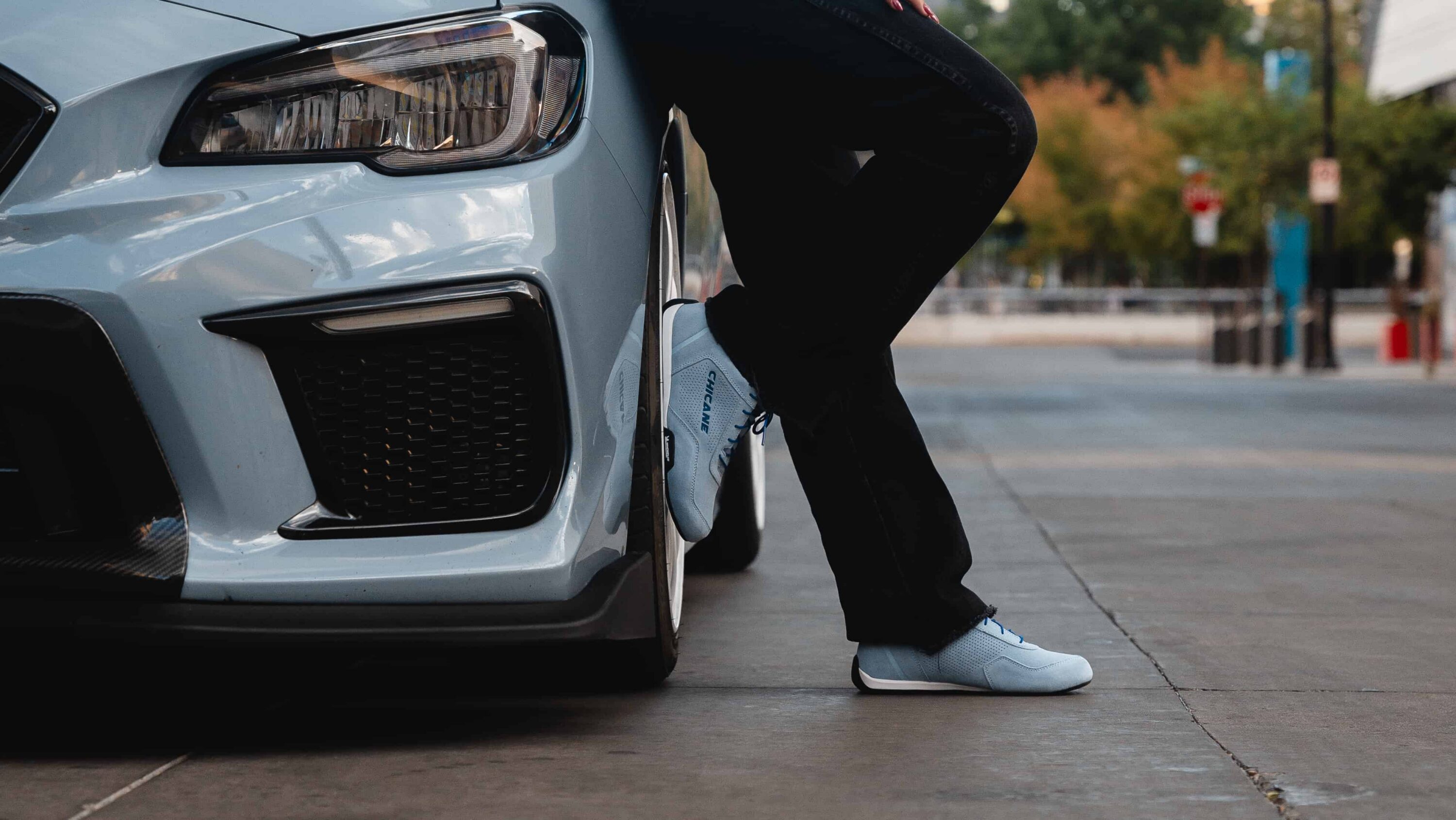 Close-up of Chicane women’s driving shoes on pedals beside sports car, emphasizing precision fit and pedal feel.