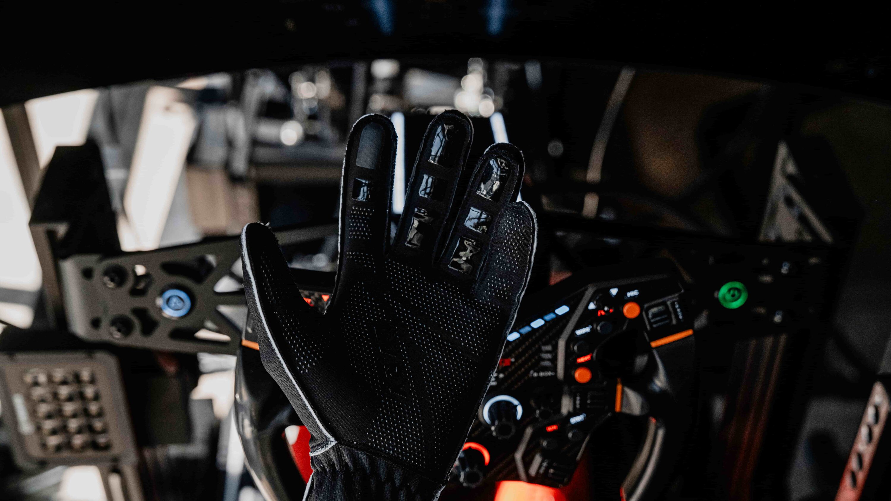 Palm view of the LVRY Sim Glove showing breathable material and grippy fingertip construction, held up in front of a full sim racing rig cockpit.