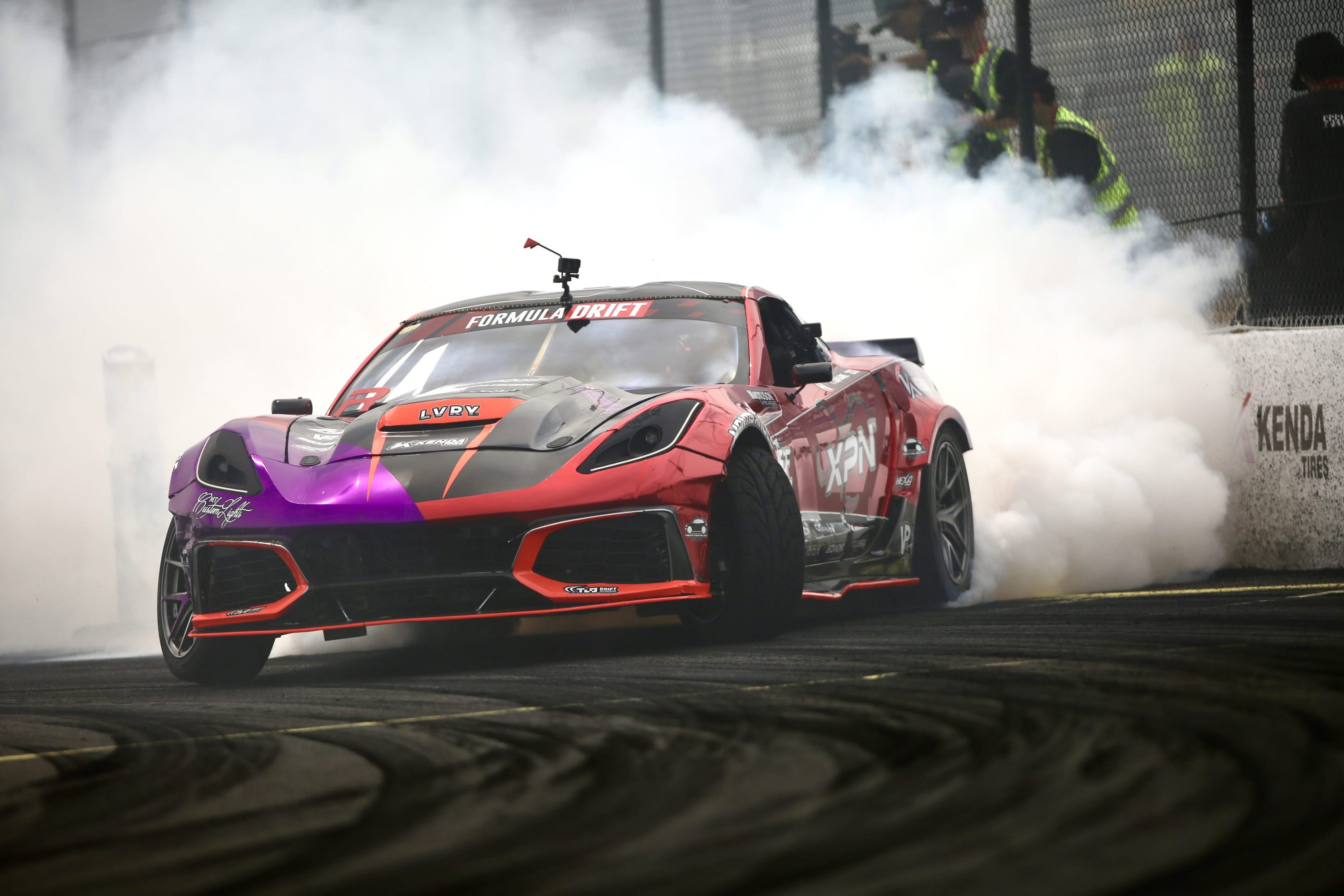 Tommy Lemaire’s red and purple Corvette C7 Formula Drift car sliding through tire smoke, LVRY logo on the hood.