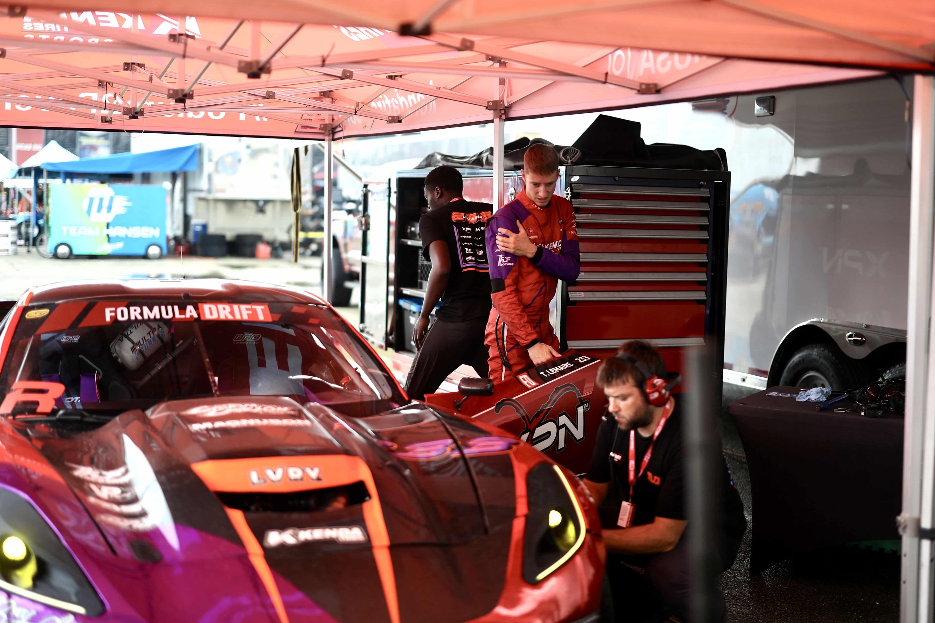 Tommy Lemaire and crew in the pits under a Kenda Tires tent, with a matching red XPN pit cart beside the Corvette C7 drift car.