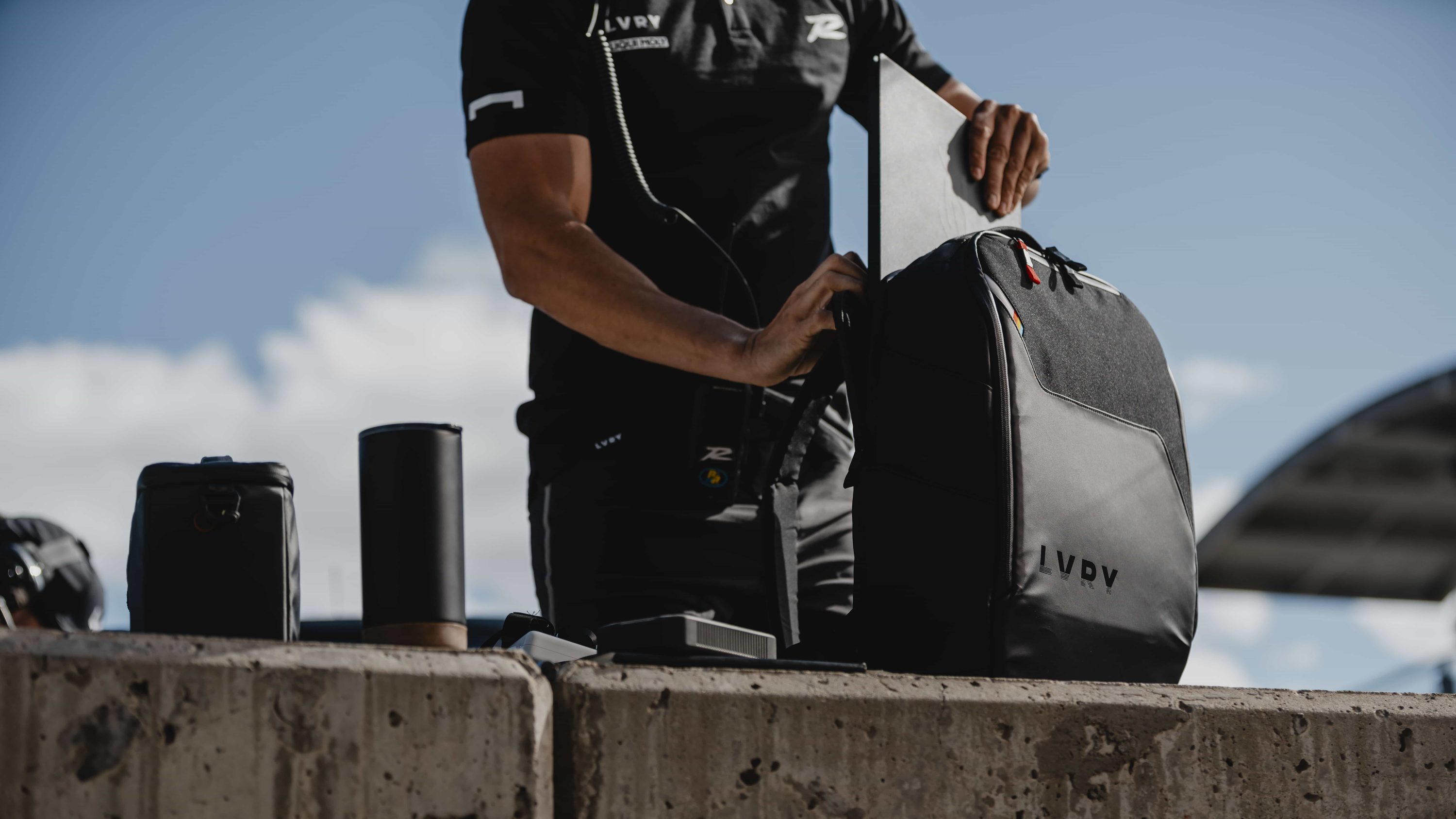 Crew member sliding a laptop into the LVRY PACK on a concrete pit wall, with a tumbler and PITBOX beside it.